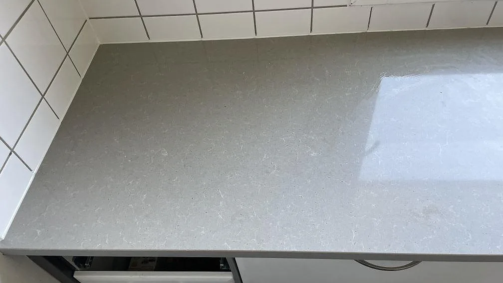 Hörn av polerad Technistone Noble Concrete Grey köksbänkskiva mot vitt kakel, med betonglik grå yta i Limhamn.