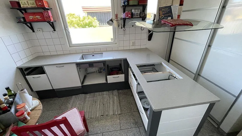 Köksbänkskiva i Technistone Noble Concrete Grey, polerad grå kvartskomposit, i ett U-format kök med halvö under montering i Limhamn.