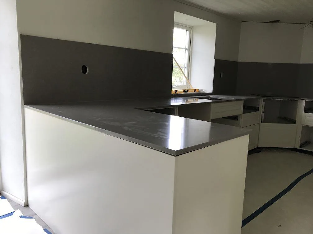 Köksbänkskiva i polerad Technistone Noble Concrete Grey i betongton, med stänkskydd längs väggen i ett ljust kök i Löberöd.