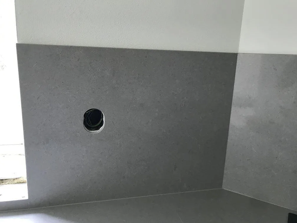 Stänkskydd i grå Technistone Noble Concrete Grey, polerad, med urtag för vägguttag i ett kök i Löberöd.