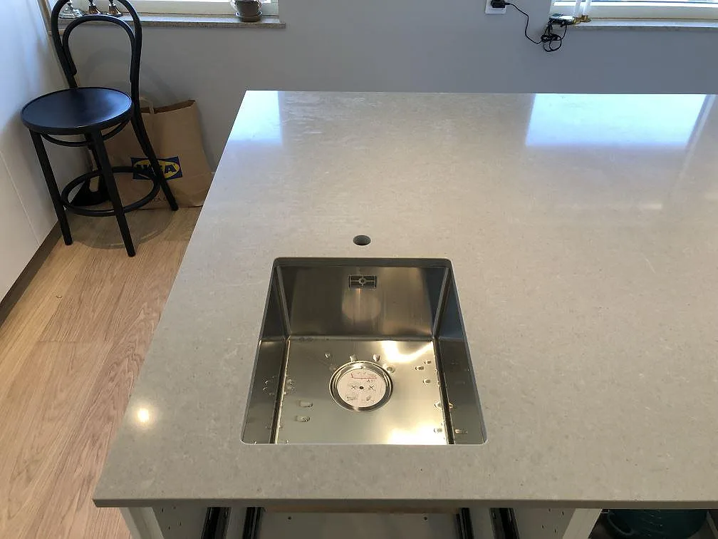Underlimmad rostfri diskho i en köksö av grå Technistone Noble Concrete Grey, polerad kvartskomposit, i Lomma.