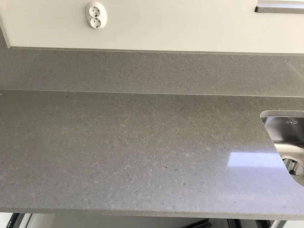 Närbild på grå Technistone Noble Concrete Grey köksbänkskiva med uppvikt stänkkant och underlimmad rostfri diskho i ett kök i Lund.