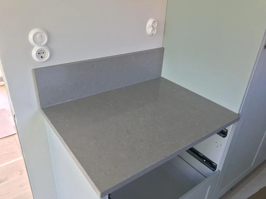 Installerad köksbänkskiva i matt grå Technistone Noble Concrete Grey med uppvikt stänkkant mot vit vägg och ljust trägolv i ett kök i Lund.
