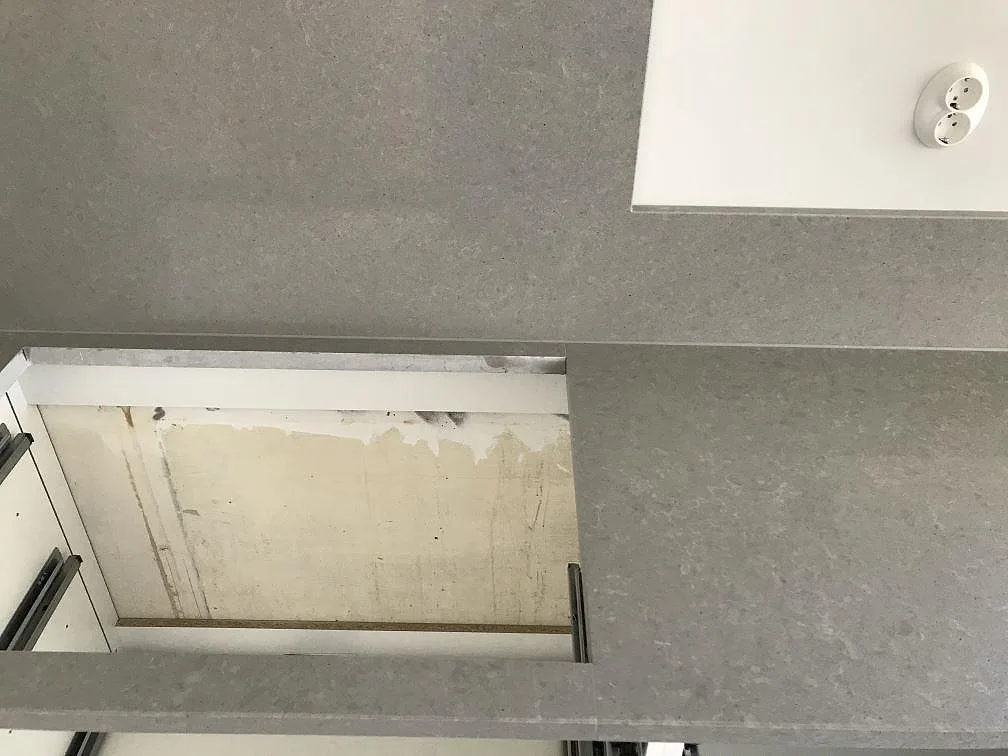 Grå Technistone Noble Concrete Grey köksbänkskiva med urtag och uppvikt stänkkant mot vit vägg i ett kök under montering i Lund.