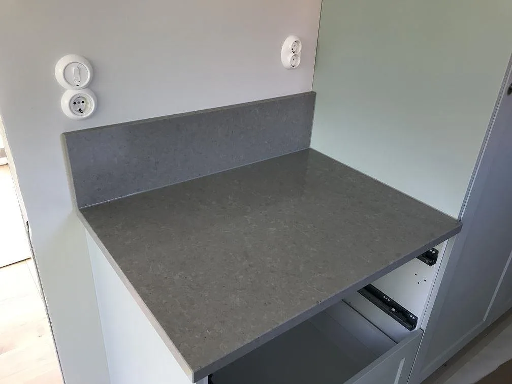 Eye-level bild på köksbänkskiva i grå Technistone Noble Concrete Grey med uppvikt stänkkant och vita skåp i ett kök under montering i Lund.