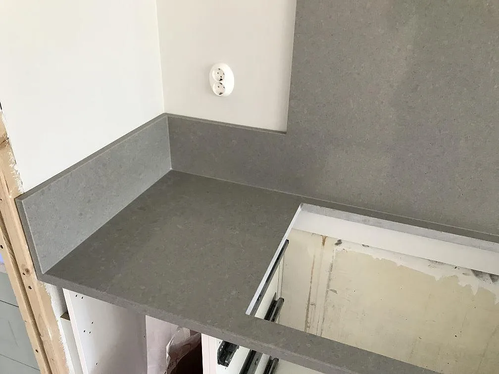 Hörnparti av grå Technistone Noble Concrete Grey köksbänkskiva med uppvikt stänkkant och urtag i ett kök under montering i Lund.