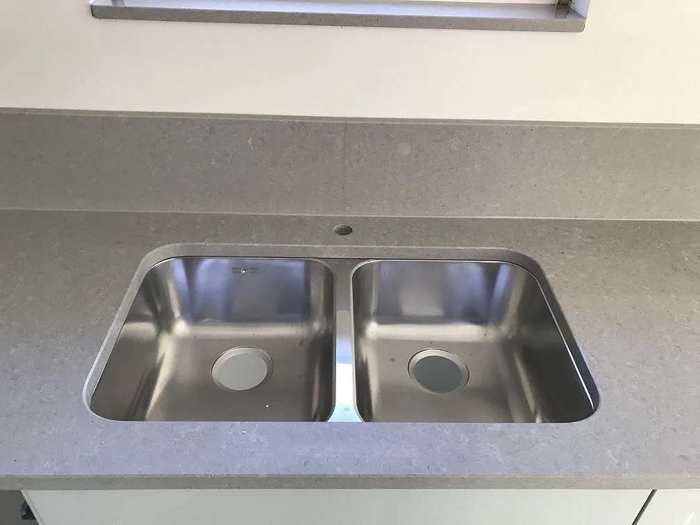 Dubbel underlimmad rostfri diskho i grå Technistone Noble Concrete Grey köksbänkskiva under ett fönster med stenfönsterbänk i ett kök i Lund.