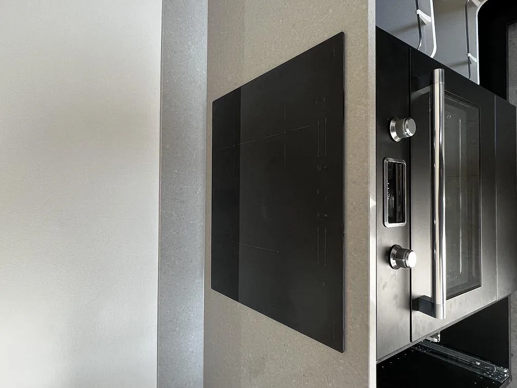 Polerad köksbänkskiva i Technistone Noble Concrete Grey med infälld induktionshäll och inbyggd ugn i ett kök i Lund.