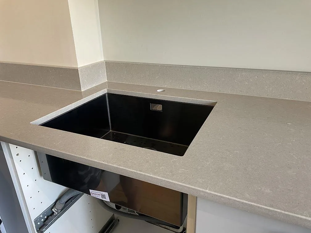 Närbild på underlimmad svart diskho i polerad Technistone Noble Concrete Grey, grå kvartskomposit med kort stänkkant i ett kök i Malmö.