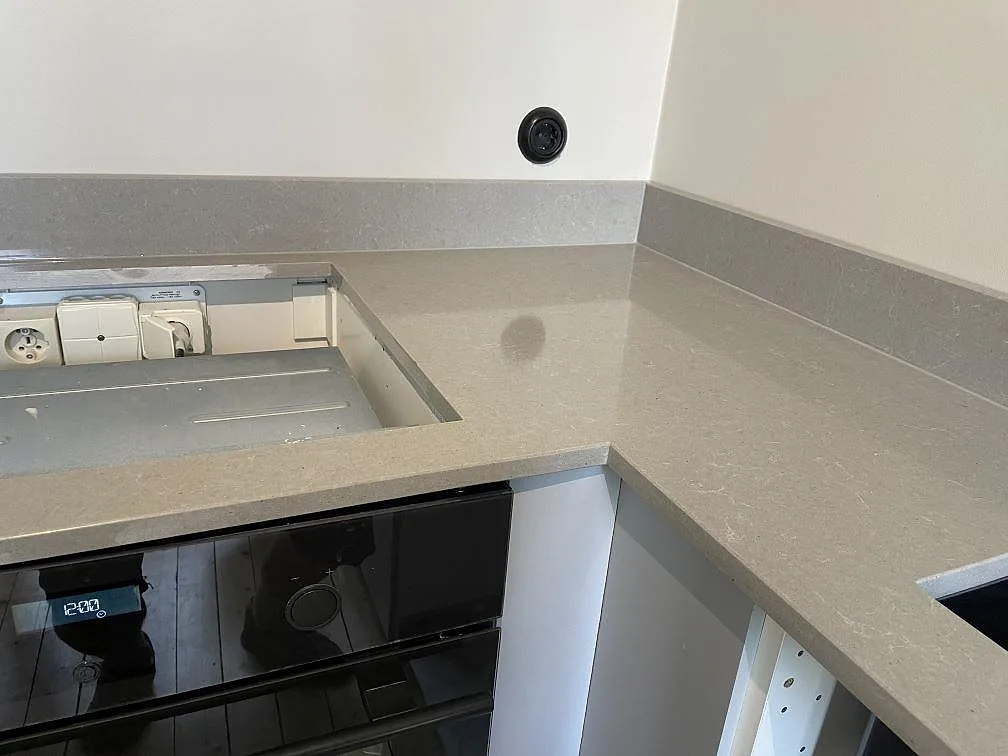 Hörn på L-formad köksbänkskiva i polerad Technistone Noble Concrete Grey med hälluttag, inbyggd ugn och stänkkant i Malmö.