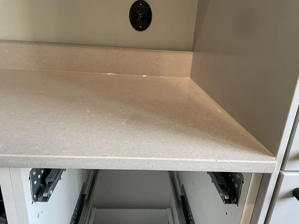 Detalj av polerad Technistone Noble Concrete Grey, ljusgrå kvartskomposit med uppvikt stänkkant och öppna stommar i ett kök i Malmö.