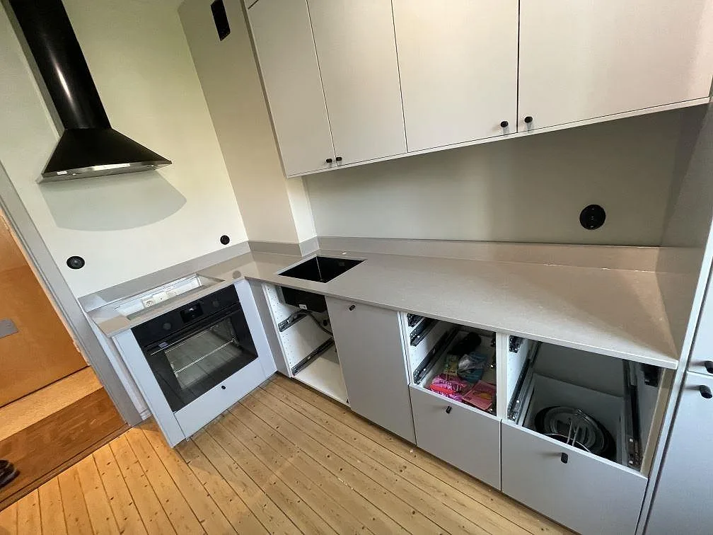 L-formad köksbänkskiva i Technistone Noble Concrete Grey, polerad grå kvartskomposit, med svart diskho, hällplats och kort stänkkant i ett kök under montering i Malmö.
