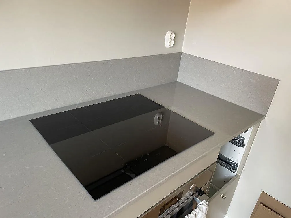 Polerad köksbänkskiva i Technistone Noble Concrete Grey med svart induktionshäll och matchande stänkskydd i ett kök i Malmö.
