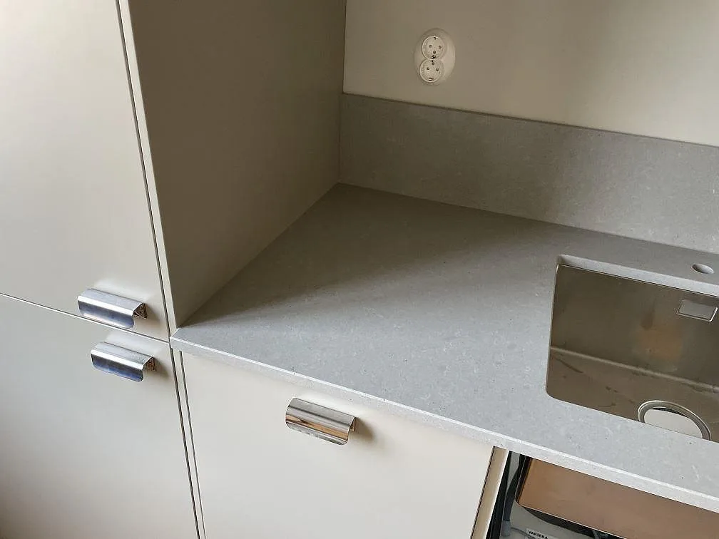 Detalj av grå Technistone Noble Concrete Grey, polerad köksbänkskiva med rostfri diskho, stänkskydd och vita köksskåp i Malmö.