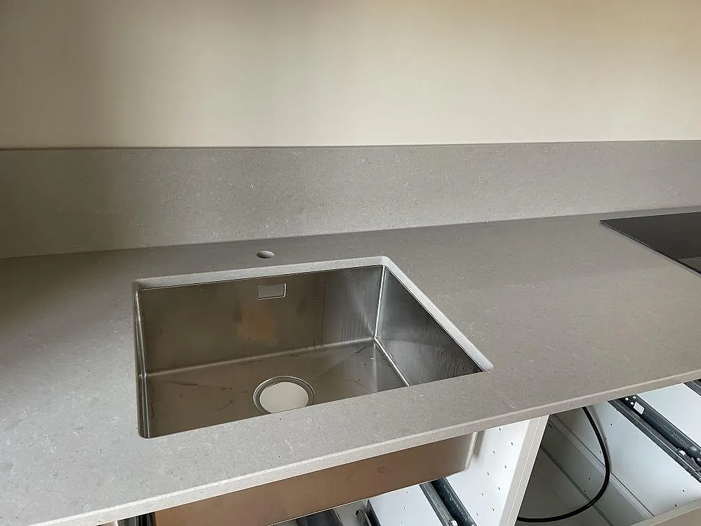 Närbild på polerad Technistone Noble Concrete Grey som köksbänkskiva med underlimmad rostfri diskho och grått stänkskydd i Malmö.