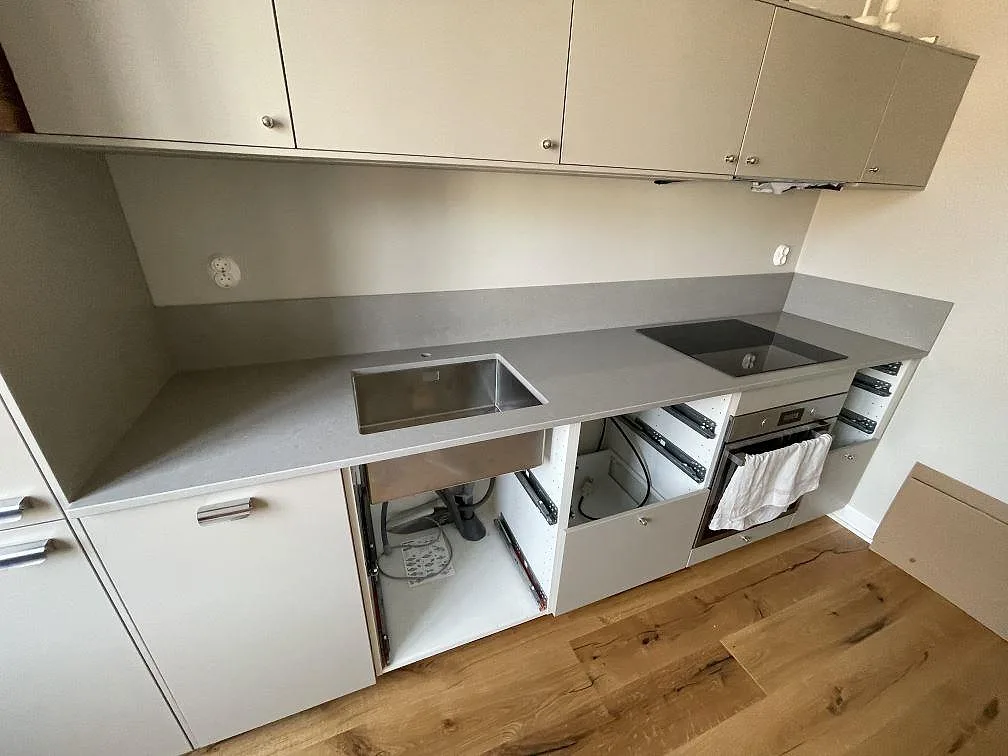 L-formad köksbänkskiva i grå Technistone Noble Concrete Grey, polerad, med stänkskydd, svart induktionshäll och rostfri diskho i Malmö.