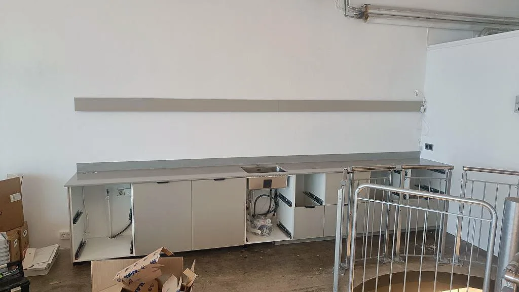 Köksbänkskiva i polerad Technistone Noble Concrete Grey med 12 mm stänkskydd och vit skåpsinredning under montering i Malmö.