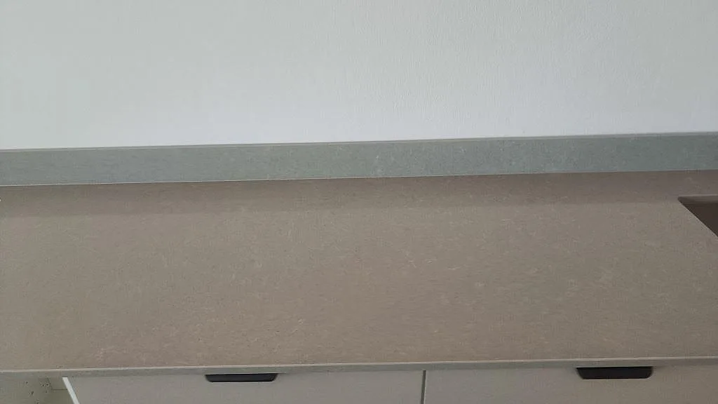 Rak detaljbild av polerad Technistone Noble Concrete Grey bänkskiva mot 12 mm stänkskydd och vita köksstommar i Malmö.