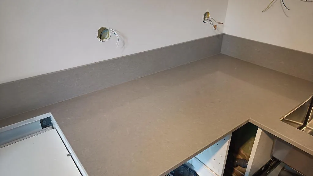 Hörnvy av polerad Technistone Noble Concrete Grey som köksbänkskiva med grått uppvikt stänkskydd och synlig struktur i Malmö.