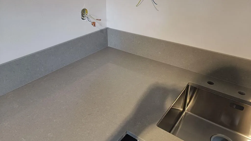 Detalj av polerad Technistone Noble Concrete Grey intill rostfri diskho och uppvikt stänkskydd i ett kök under montering i Malmö.
