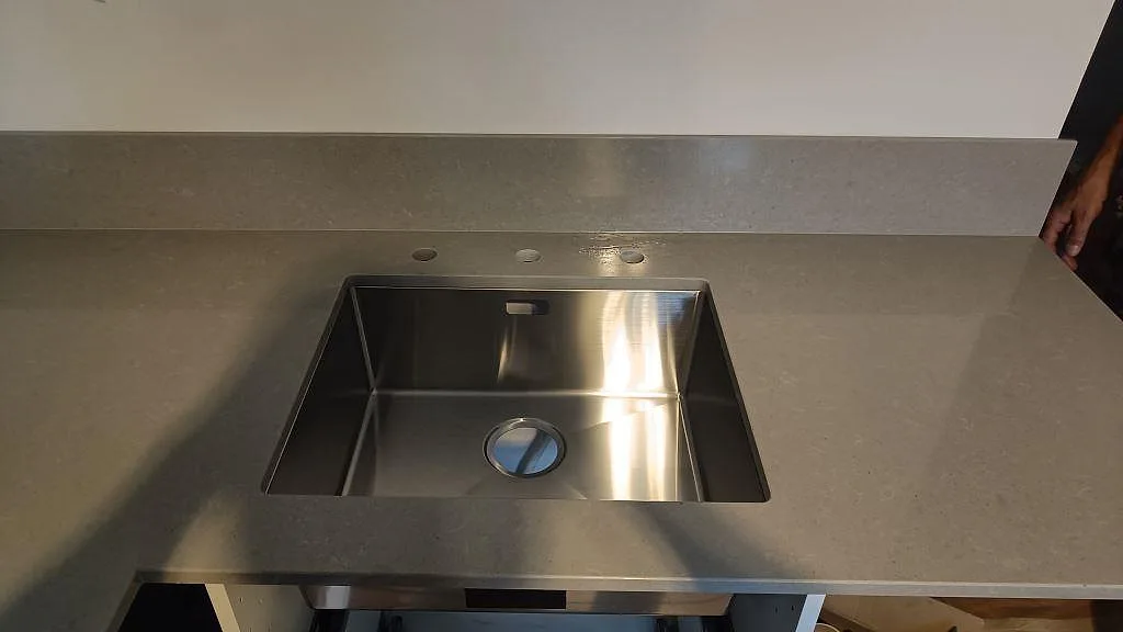 Rostfri diskho vid en polerad köksbänkskiva i Technistone Noble Concrete Grey med matchande grått stänkskydd i Malmö.