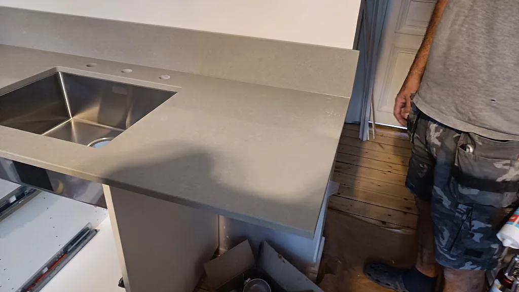 Sidovy av grå polerad Technistone Noble Concrete Grey köksbänkskiva med rostfri diskho och uppvikt stänkskydd i Malmö.