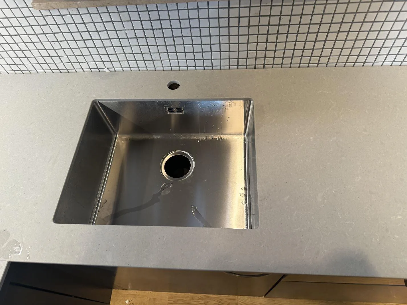 Rostfri diskho i en matt grå Technistone Noble Concrete Grey köksbänkskiva med mosaikkakel bakom i Malmö.