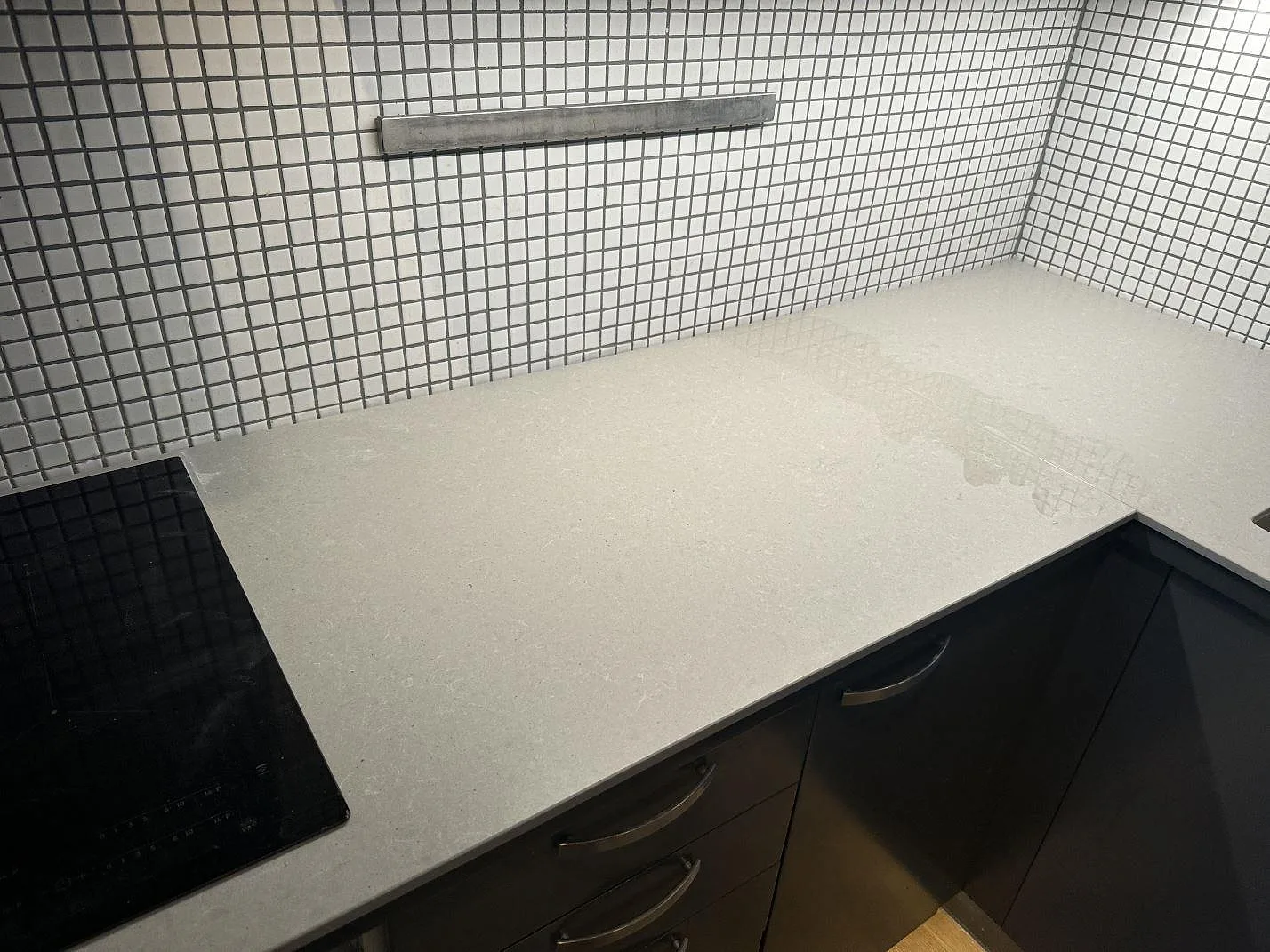 Närbild av matt Technistone Noble Concrete Grey som köksbänkskiva vid svart häll och mörka underskåp i ett kök i Malmö.