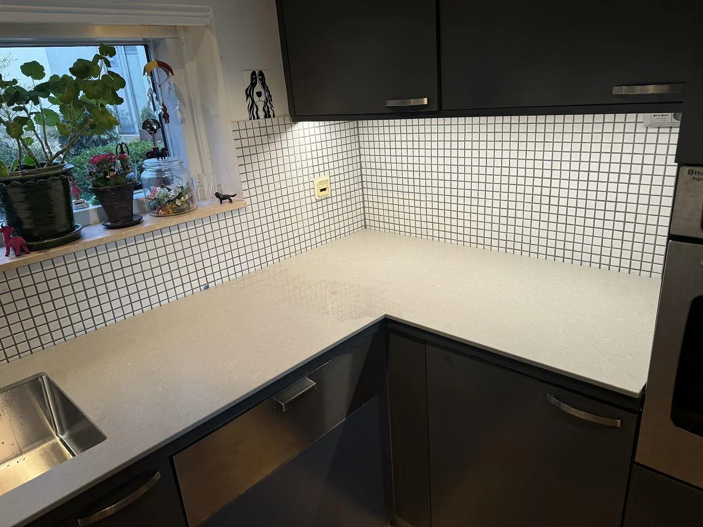 Matt grå köksbänkskiva i Technistone Noble Concrete Grey runt ett hörn med mosaikkakel, mörka luckor och rostfri diskho i Malmö.
