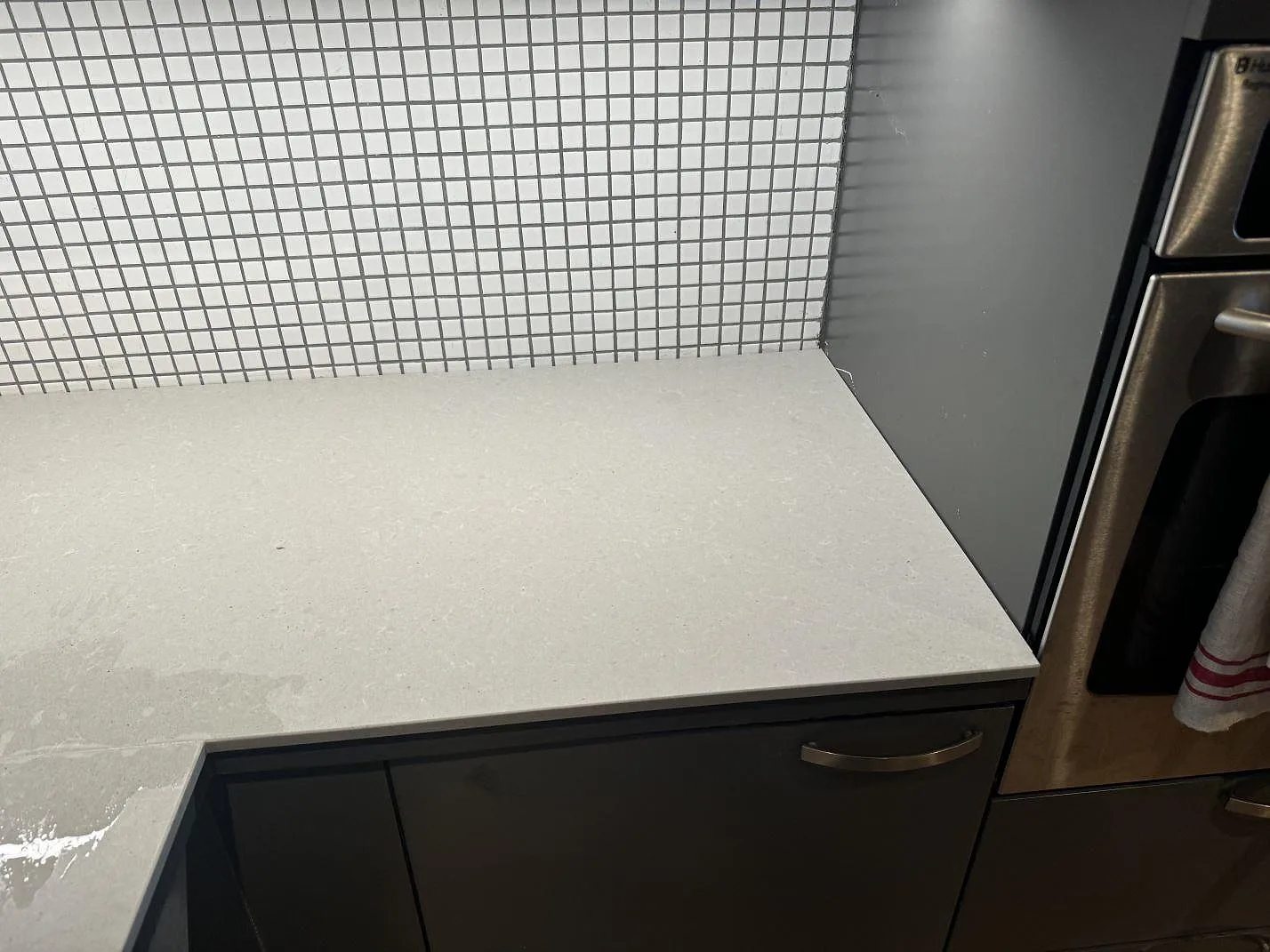 Detalj av matt Technistone Noble Concrete Grey köksbänkskiva mot mörka skåp, väggugn och mosaikkakel i Malmö.