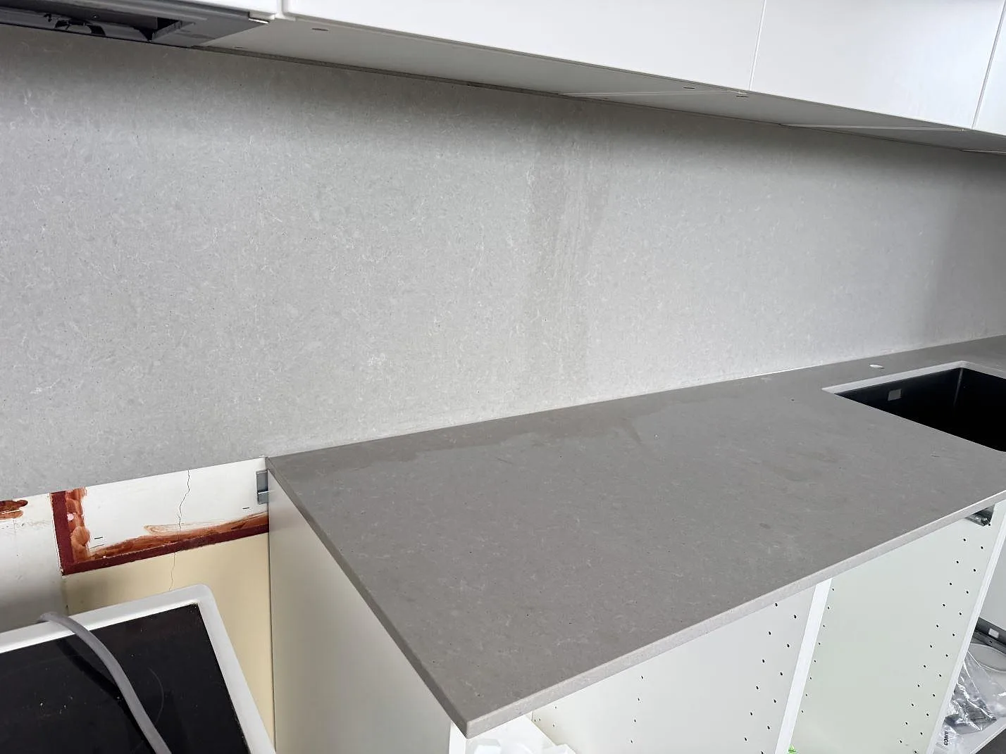 Lång köksbänkskiva i matt Technistone Noble Concrete Grey med grå väggbeklädnad och öppna köksstommar under montering i Malmö.