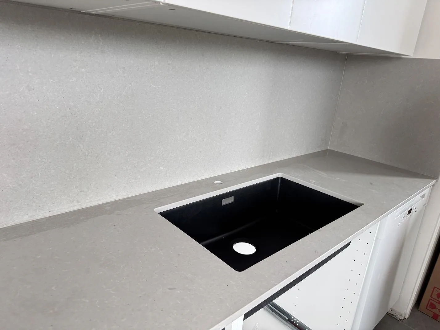 Köksbänkskiva i matt Technistone Noble Concrete Grey, grå kvartskomposit, med svart diskho och matchande stänkvägg i ett kök i Malmö.