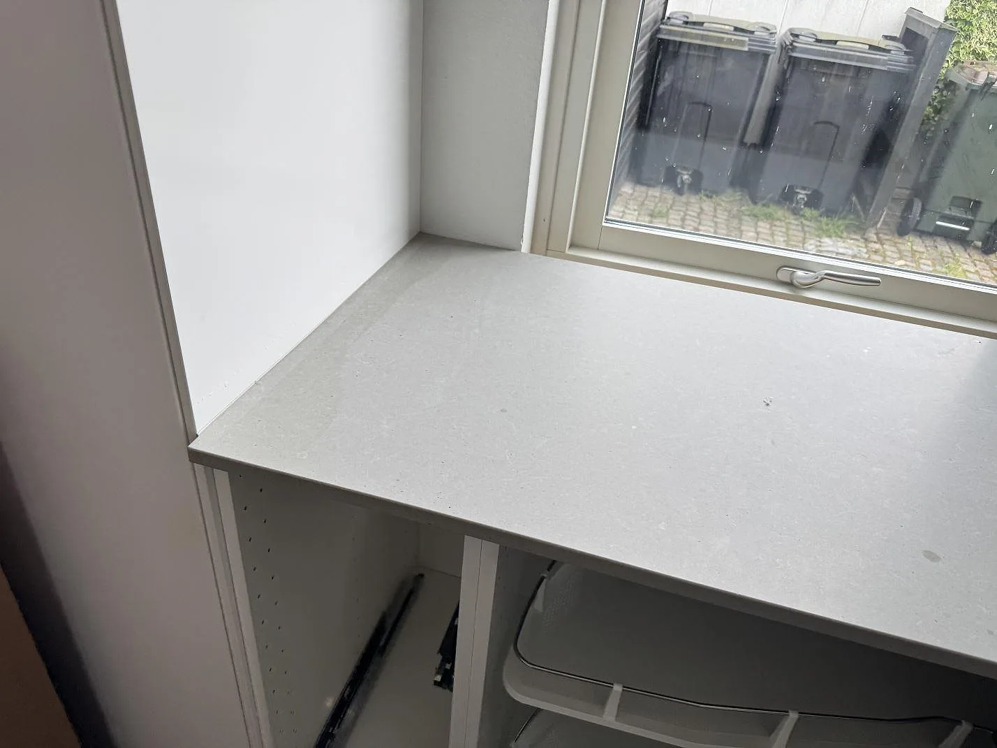 Arbetsyta vid fönster i matt Technistone Noble Concrete Grey, grå kvartskomposit, monterad på vita stommar i Malmö.