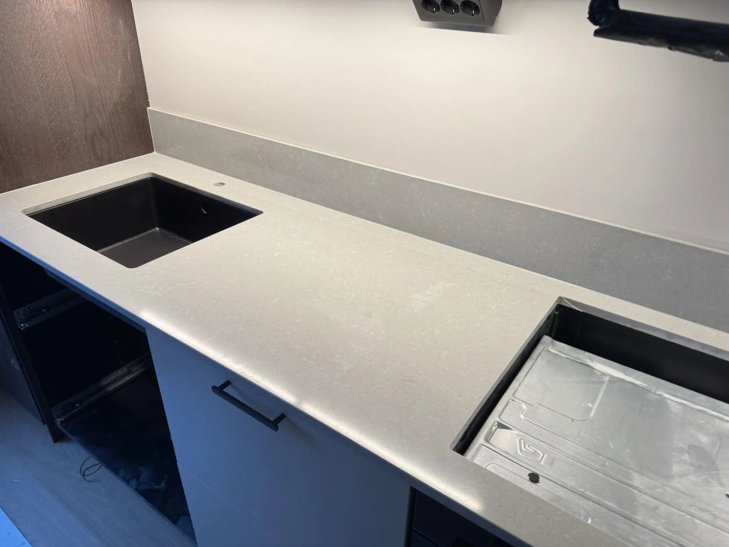 Grå köksbänkskiva i Technistone Noble Concrete Grey med underlimmad svart komposithoar och uppvikt stänkkant mot träsida i ett kök i Malmö.