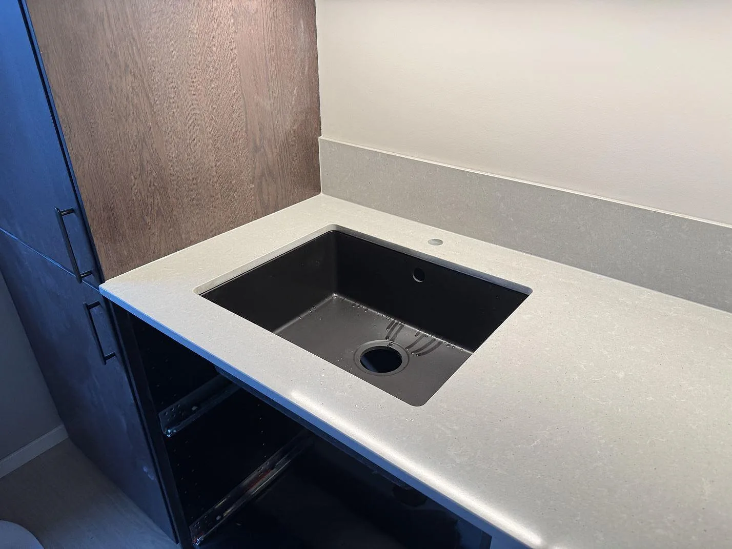 Detalj av underlimmad svart komposithoar med borrat blandarhål i grå Technistone Noble Concrete Grey, polerad köksbänkskiva i Malmö.