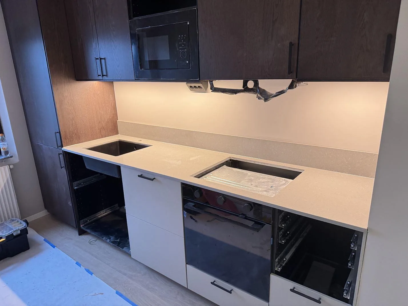Översikt över ett kök i Malmö under montering med köksbänkskiva i Technistone Noble Concrete Grey, mörka träöverskåp och uppvikt stänkkant i samma grå komposit.