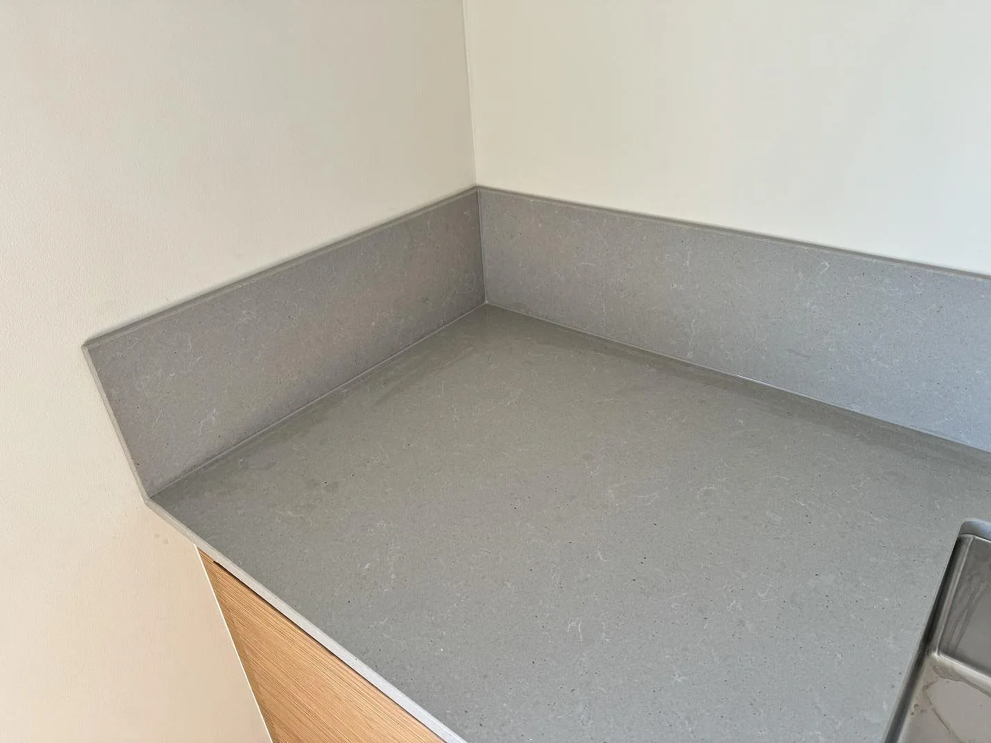 Hörndetalj av matt Technistone Noble Concrete Grey köksbänkskiva med uppvikt stänkskydd och rostfri diskho i Mölndal.
