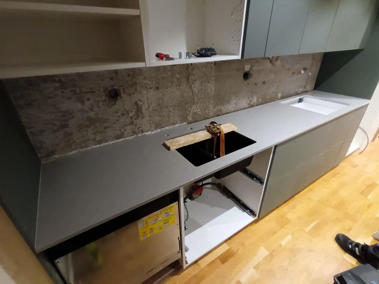 Köksbänkskiva i Technistone Noble Concrete Grey, polerad grå kvartskomposit, under montering i ett kök med gröna stommar i Motala.