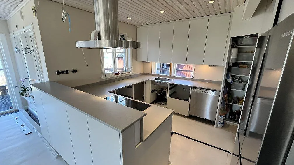 Vidvinkelbild av kök i Norrby med matt Technistone Noble Concrete Grey som bänkskiva på halvö, hällzon och väggbänkar.