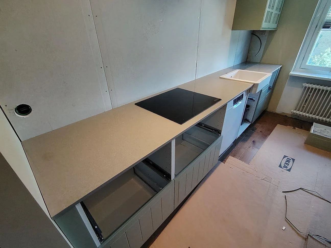 Polerad köksbänkskiva i grå Technistone Noble Concrete Grey, 20 mm kvartskomposit, med häll och diskho i ett vitt kök under montering i Nyköping.