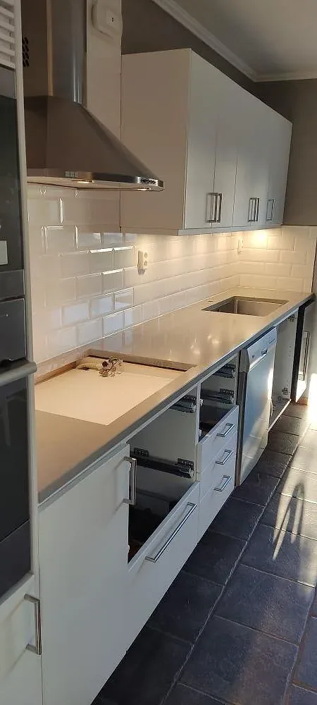 Köksbänkskiva i grå betonglik Technistone Noble Concrete Grey med nedsänkt diskho, mot vitt tegelkakel och vita luckor i ett kök i Skövde.