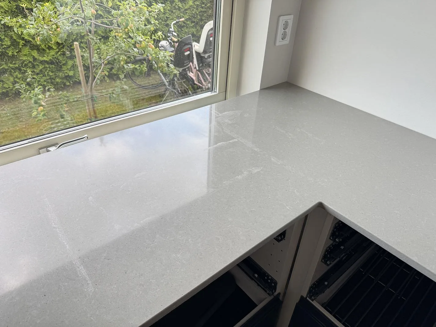 Polerad kvartskomposit i Technistone Noble Concrete Grey som köksbänkskiva runt ett fönsterhörn i Svalöv.