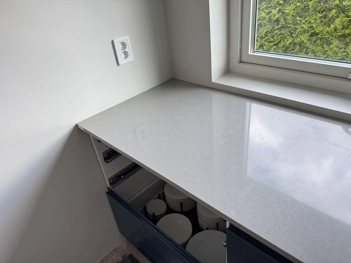 Köksbänkskiva i polerad Technistone Noble Concrete Grey under fönster med mörka underskåp i Svalöv.