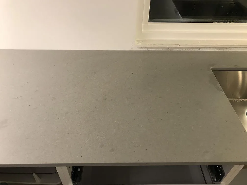 Lång köksbänkskiva i grå Technistone Noble Concrete Grey med underlimmad rostfri diskho under fönstret i ett kök i Svedala.