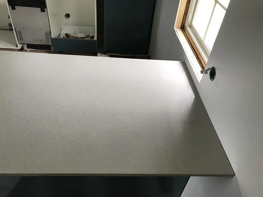 Närbild ovanifrån på den finkorniga grå ytan på en polerad Technistone Noble Concrete Grey köksbänkskiva i ett kök i Träslövsläge.