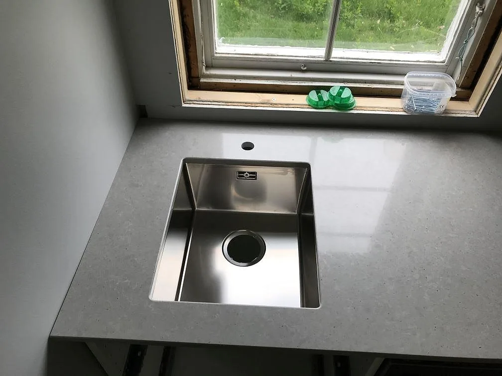 Underlimmad rostfri diskho i en polerad Technistone Noble Concrete Grey köksbänkskiva intill fönstret i ett kök i Träslövsläge.