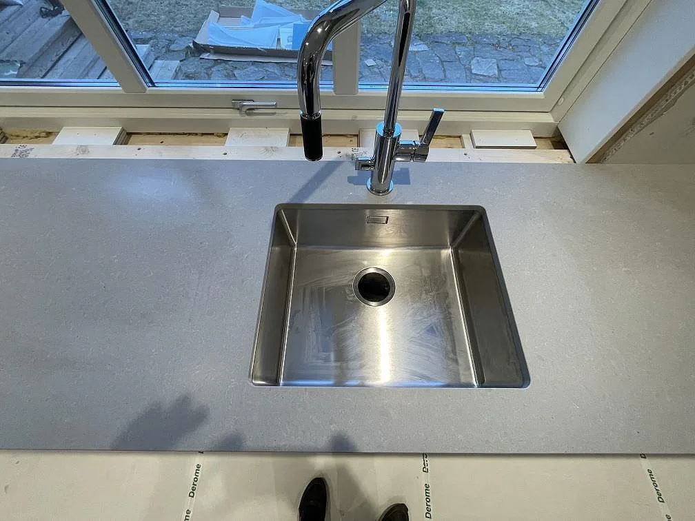 Närbild på underlimmad rostfri diskho och kromblandare i en matt grå Technistone Noble Concrete Grey köksbänkskiva i Värnamo.
