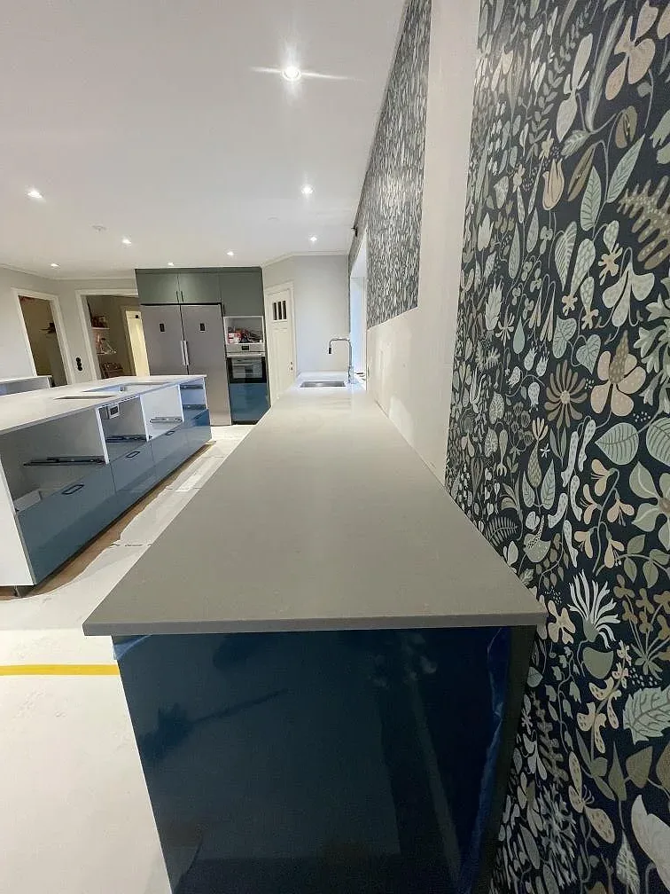 Köksö i matt grå Technistone Noble Concrete Grey med mörkblå skåp och blommig tapet i ett kök under montering i Värnamo.