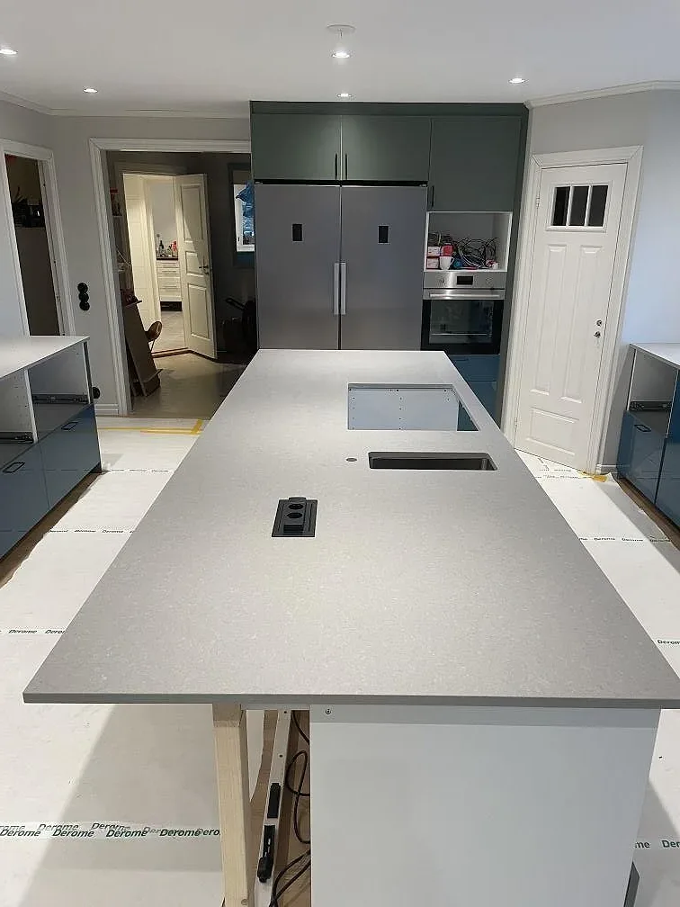 Köksö i matt grå Technistone Noble Concrete Grey med gröna skåp och rostfritt kylskåp i ett kök under montering i Värnamo.