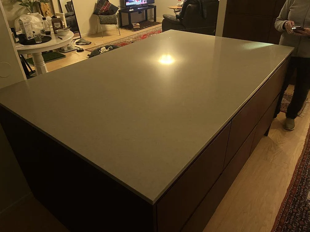 Stor köksö med polerad Technistone Noble Concrete Grey i mörk kvartskomposit och träinredning i Västerås.